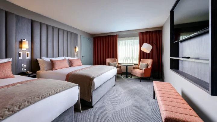 Spacious modern room with two plush double beds, relaxing seating area, large TV, and elegant lighting.
