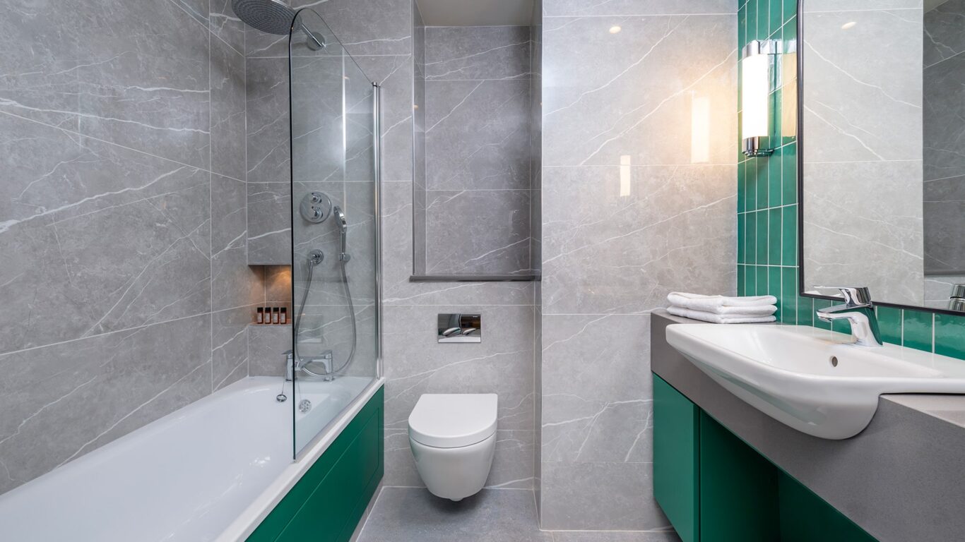 Modern hotel bathroom with glass shower, stylish green accents, and plush towels, offering a relaxing stay near city centre.