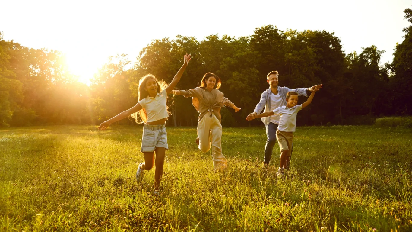 Family enjoying a sunny meadow, experiencing joyful outdoor activities near a lush forest at a welcoming family-friendly hotel.