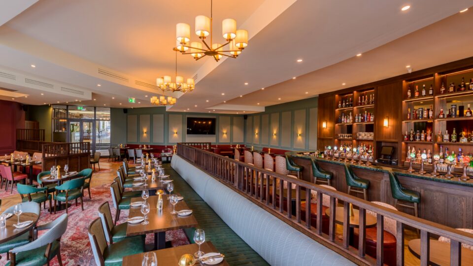 Elegant hotel restaurant with warm lighting, modern d&eacute;cor, cosy seating, and a stocked bar offering a welcoming dining experience.