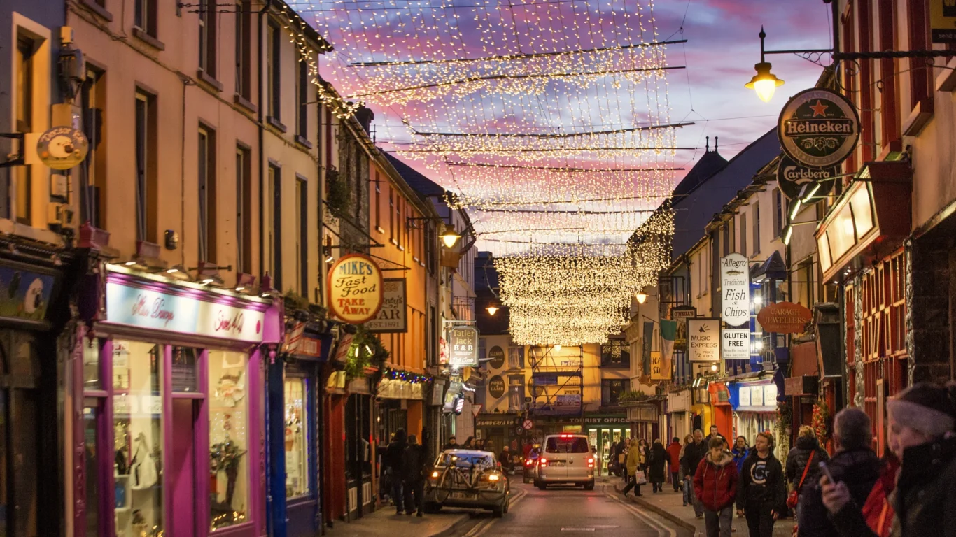 Charming evening street scene with festive lights, colourful shopfronts, and lively atmosphere in picturesque hotel area.
