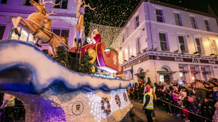 Festive parade with Santa's sleigh and reindeer, illuminated holiday lights, and joyful crowd at a lively city event.