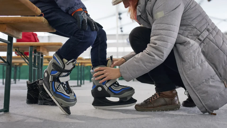 Guests enjoy an indoor ice skating rink as a woman helps a child with skates, offering a fun family-friendly hotel experience.