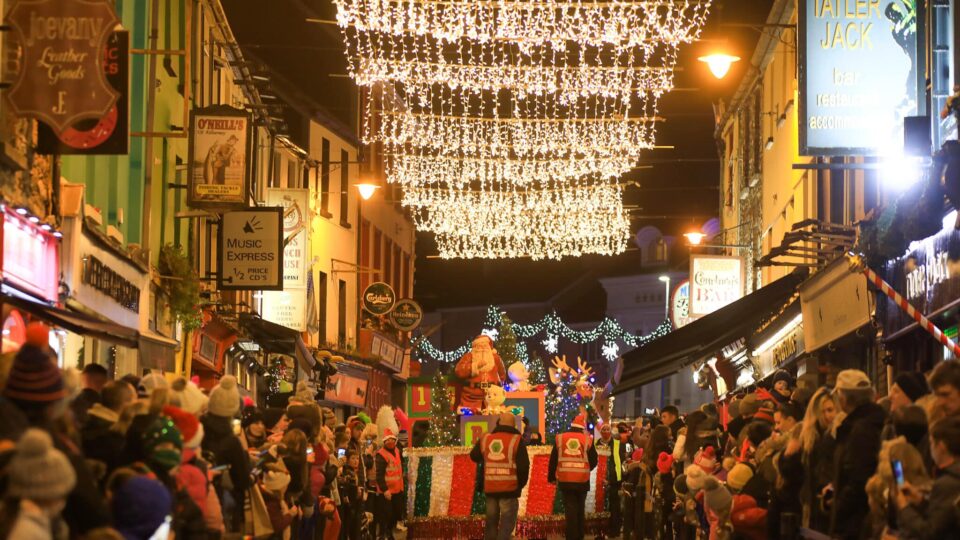 Lively nighttime Christmas parade with festive lights and cheerful crowd by Tatler Jack Hotel, creating a magical atmosphere.