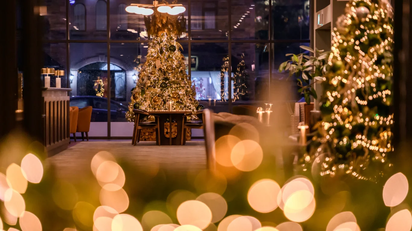 A decorated lobby with Christmas trees, festive lights, and blurred golden bokeh in the foreground.