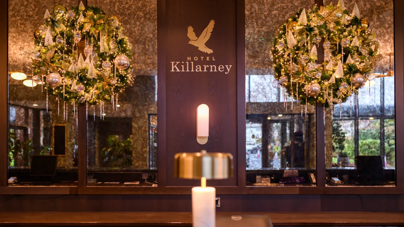 Hotel Killarney lobby with two large decorated wreaths, a central wall sconce, and a gold lamp on a polished counter.