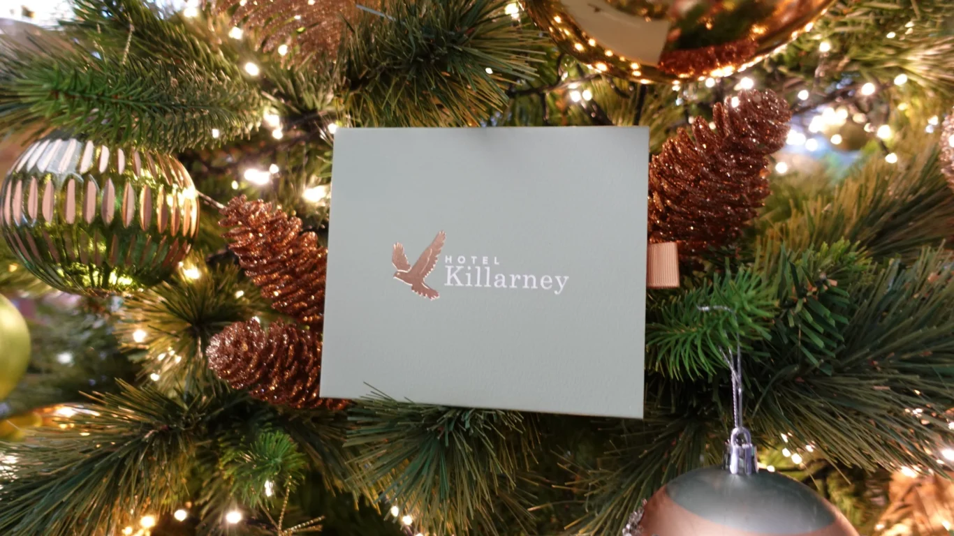 A Hotel Killarney card is displayed on a Christmas tree decorated with lights, baubles, and glittery pinecones.